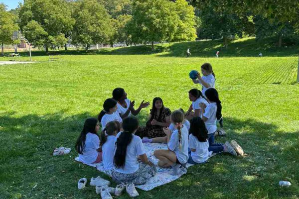 Kinder und Erwachsene lauschen einer Frau auf einer Picknickdecke im sonnigen Park auf der Wiese.